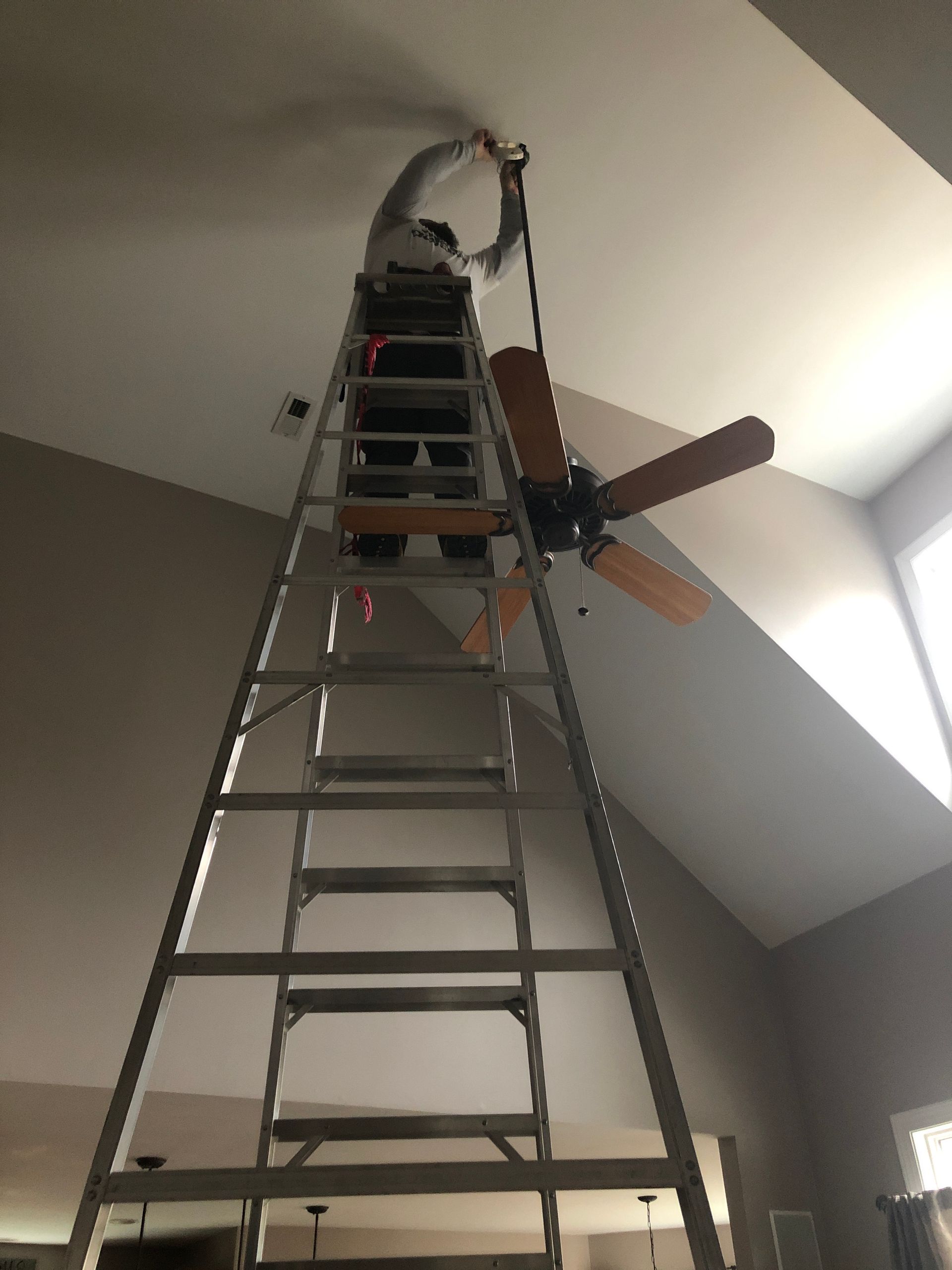 a man is on a ladder working on a ceiling fan