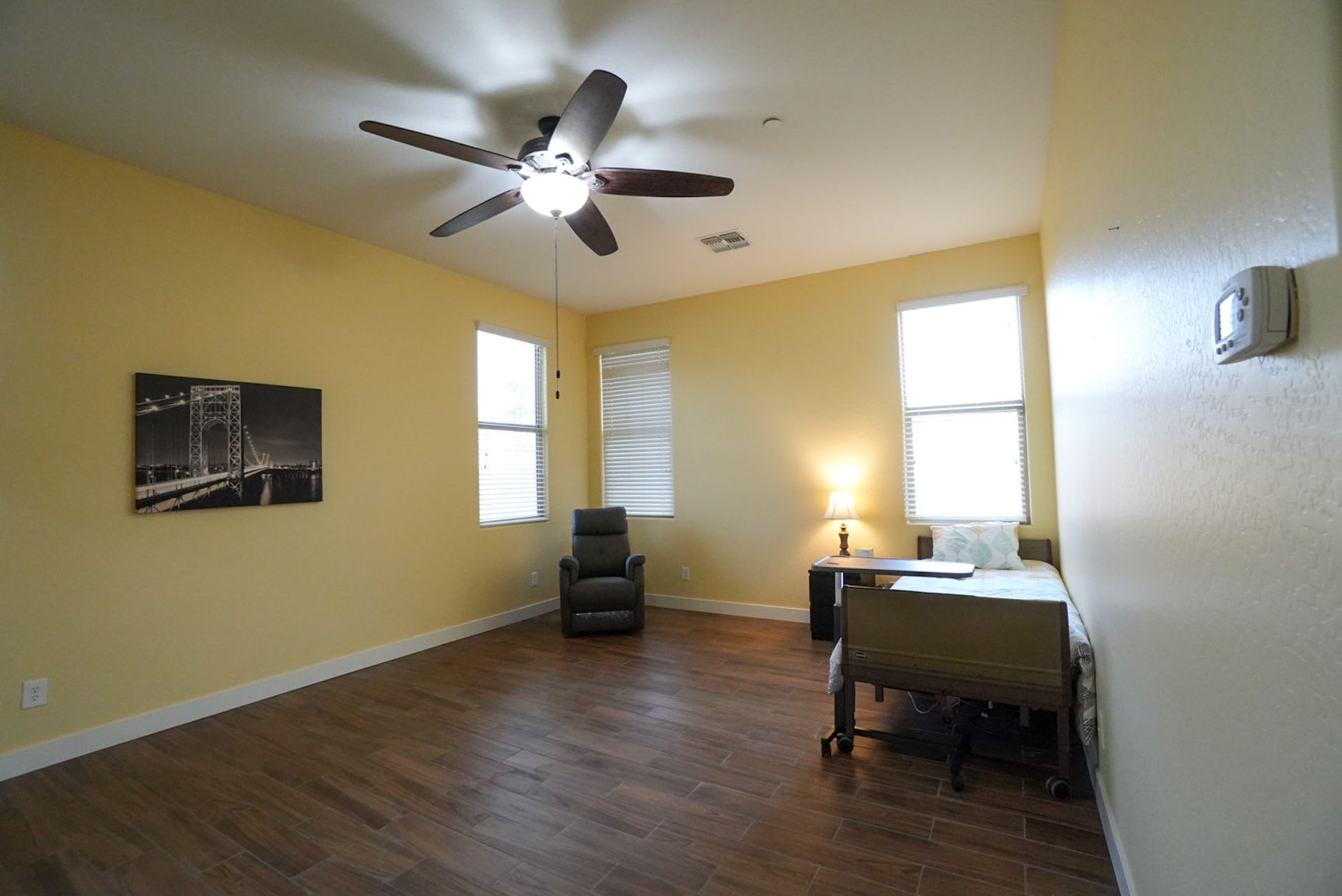Empty room with wood floor, yellow walls, ceiling fan, windows, and a desk.