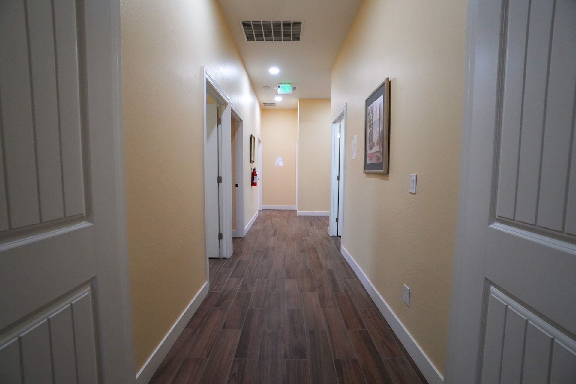 Hallway with wooden floor, cream walls, and white doors. A framed picture hangs on the right.