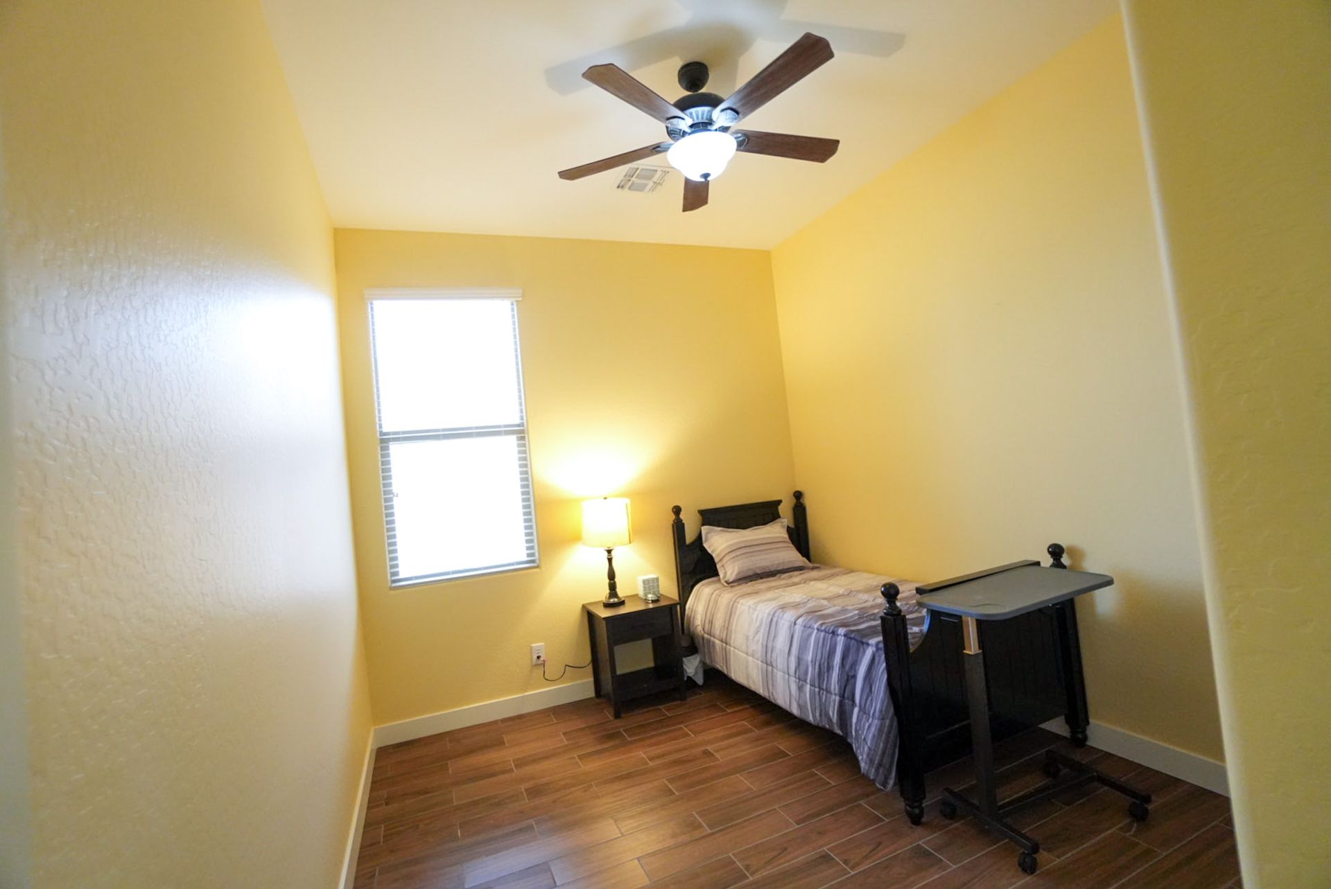 Small bedroom with yellow walls, window, bed, nightstand, and ceiling fan.
