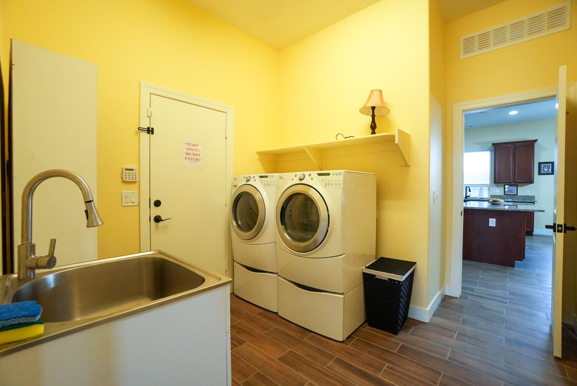 Yellow laundry room with a washer/dryer, sink, and door leading to a kitchen.