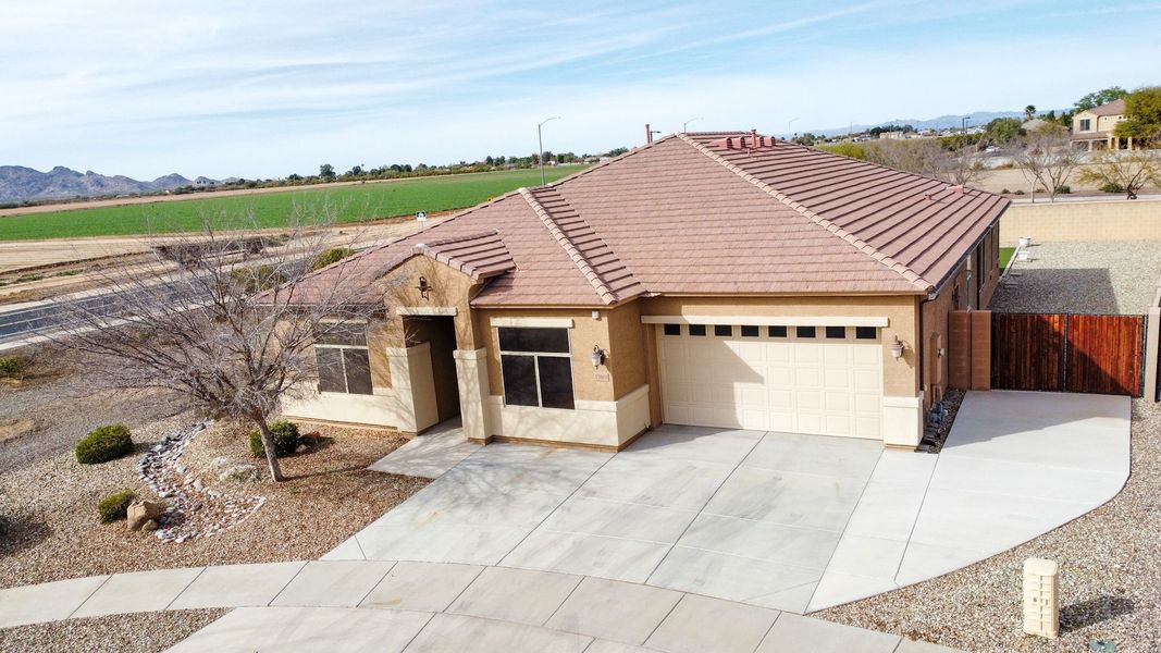 Tan single-story house with a concrete driveway and a brown tile roof, desert landscape background.