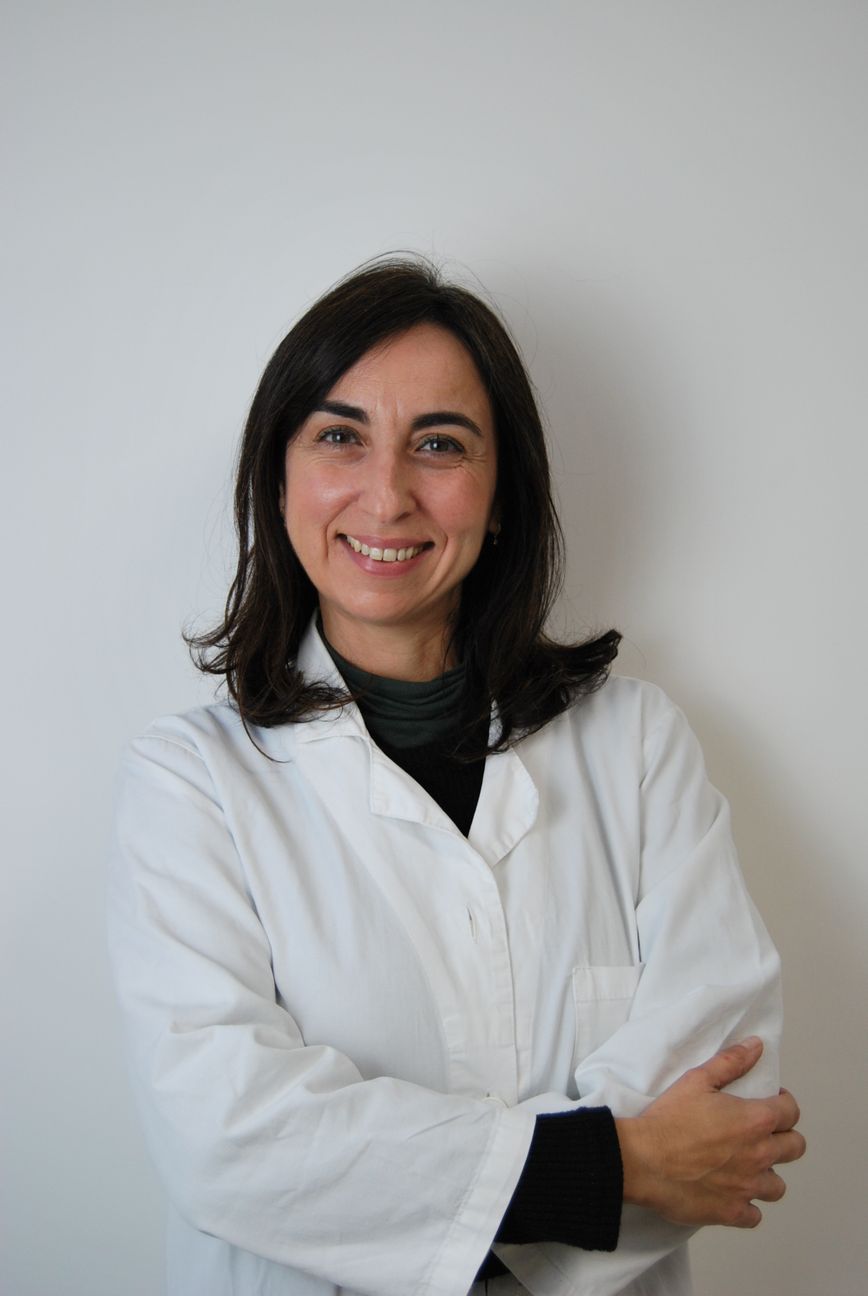 Una donna in camice bianco sorride con le braccia incrociate