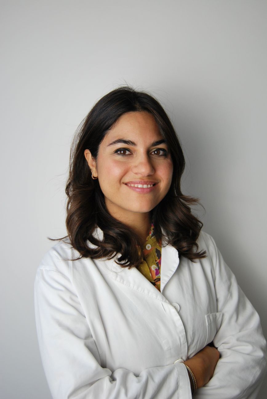 Una donna con camice bianco sorride con le braccia incrociate.