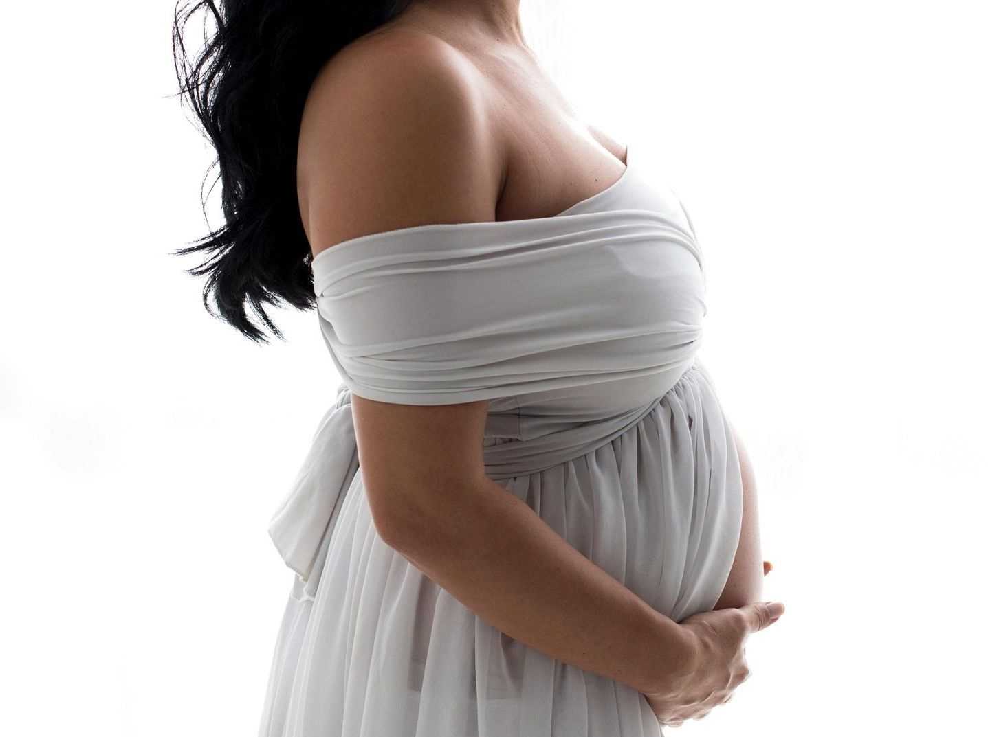 Una donna incinta vestita di bianco si tiene la pancia.