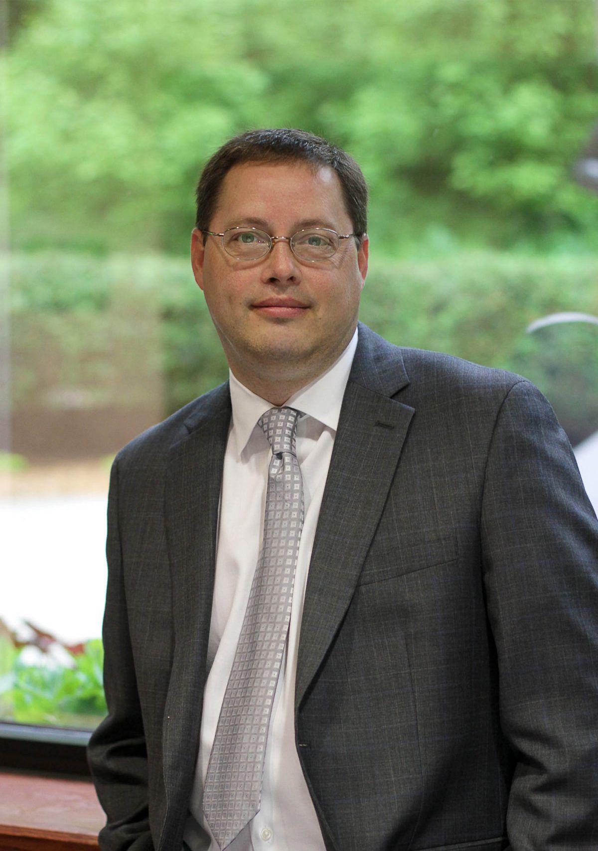 A man in a suit and tie is standing in front of a window.