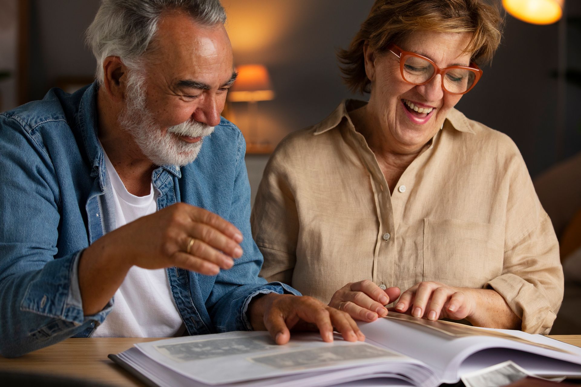 Older couple smiles while looking at a photo album together indoors.