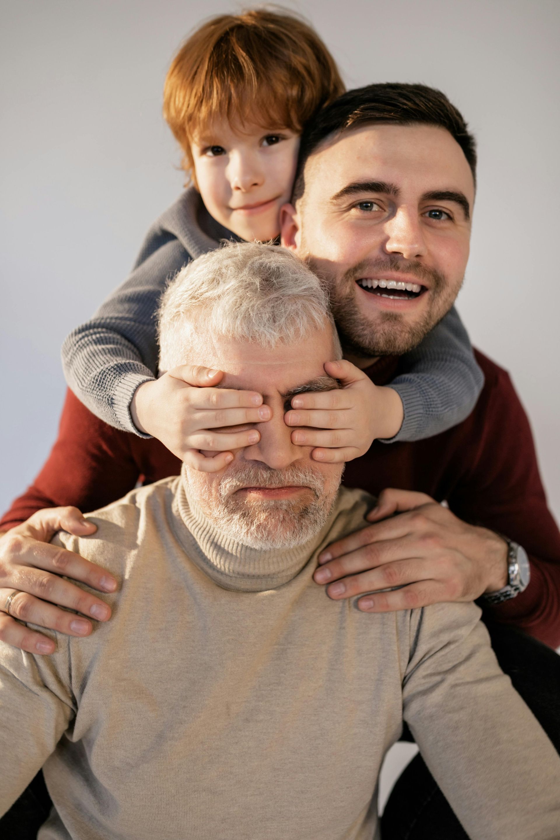 A little boy is covering an older man 's eyes with his hands.