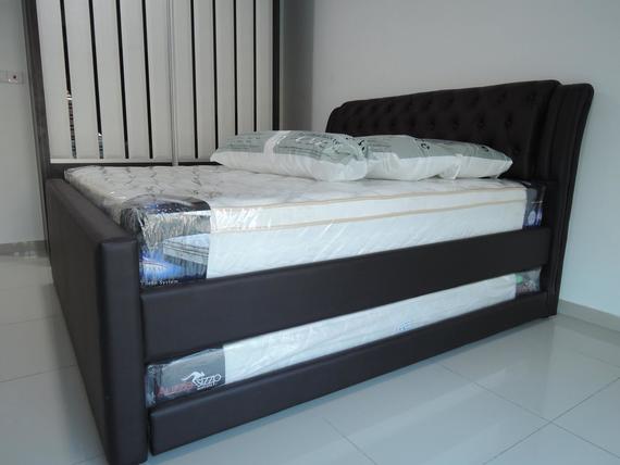 Brown upholstered bed with a tufted headboard, two pillows, and a mattress in a bright room.