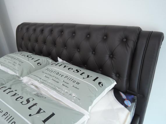 Dark brown tufted headboard with light green pillows.