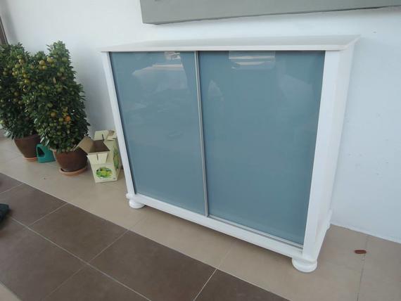 White cabinet with blue-tinted sliding glass doors, sitting on a brown tiled floor.
