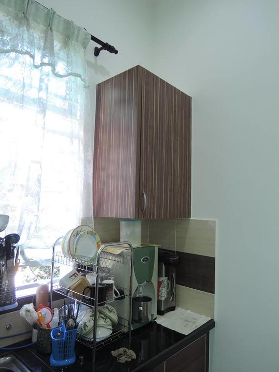 Kitchen corner with hanging cabinet, dishes on a rack, coffee maker, and window with curtains.