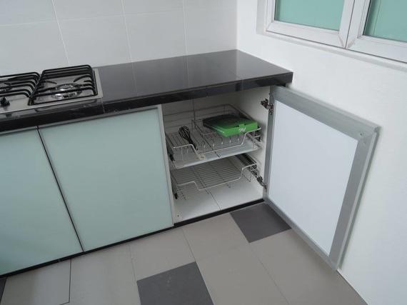 A kitchen cabinet with the door open, showing a pull-out wire rack with utensils and a cleaning sponge.