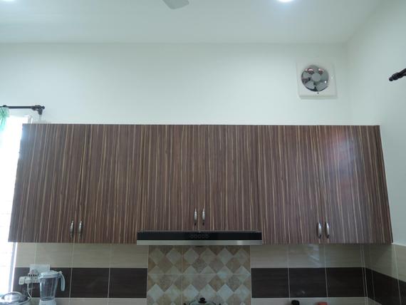 Brown kitchen cabinets above a tiled backsplash, with a range hood and a fan in the wall.