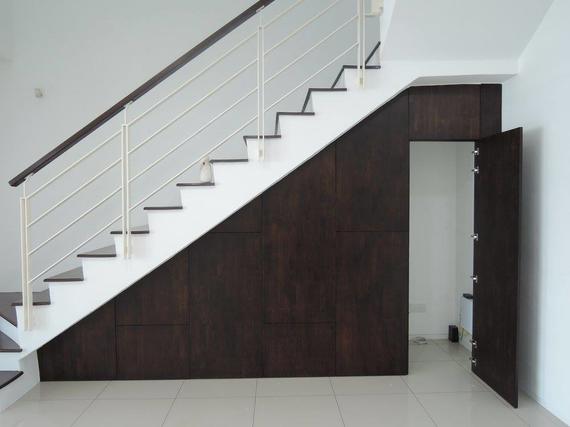 Staircase with dark wood storage underneath and open door, white walls, and metal railing.