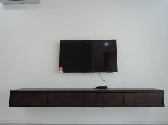 A flat-screen TV mounted on a white wall above a floating, dark-wood cabinet.