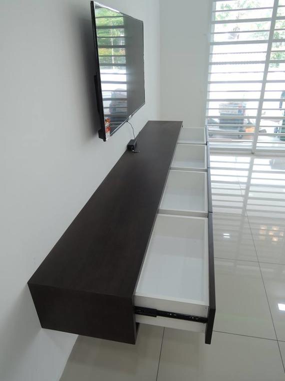 A dark brown wall-mounted TV console with three open white drawers, and a TV above.