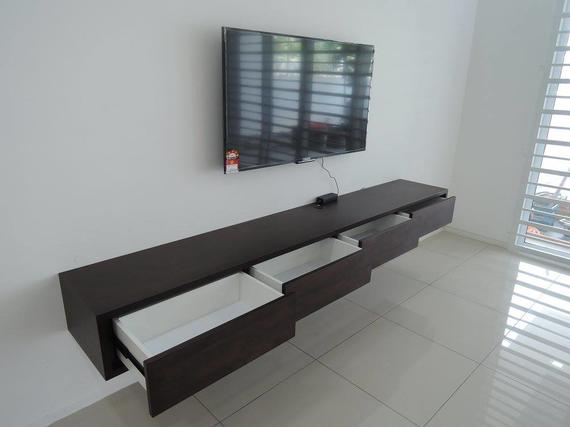 A dark floating entertainment unit with open drawers beneath a mounted TV on a white wall.