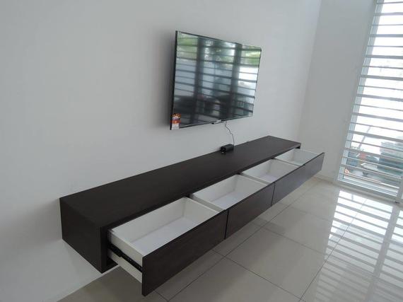 Wall-mounted TV above a dark brown floating console with three open white drawers. White wall and floor with window.
