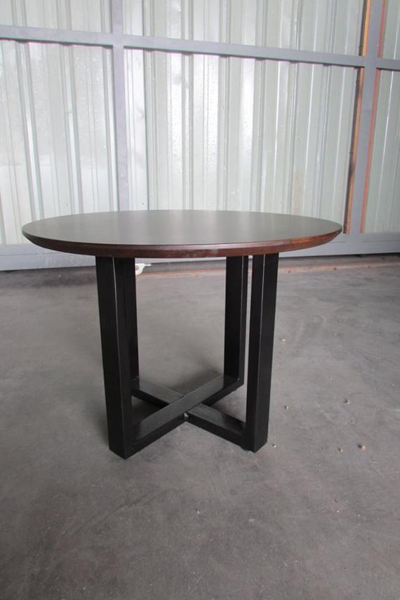 Round wooden table with dark brown top and black, crossed-leg base; indoors.