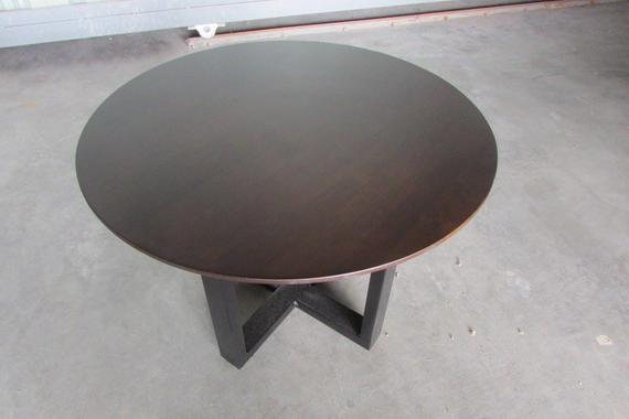 Round, dark-brown coffee table with a dark, cross-shaped base on a gray surface.