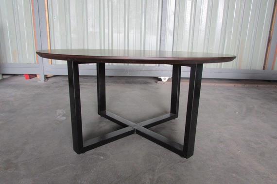 Round wooden table with dark brown top and black metal legs, in an industrial setting.