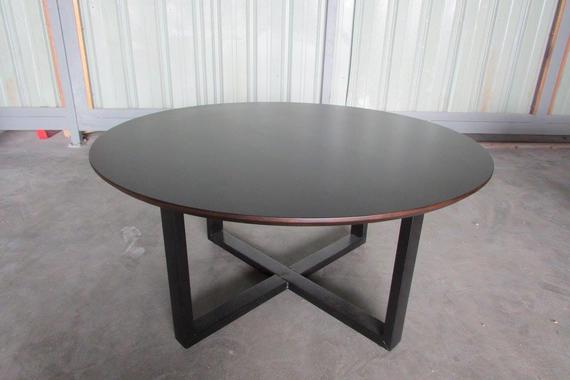 Dark brown round coffee table with an X-shaped black base in a neutral setting.