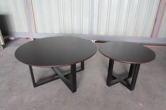 Two round, dark brown coffee tables with black cross-legged bases, in front of a light-colored wall.