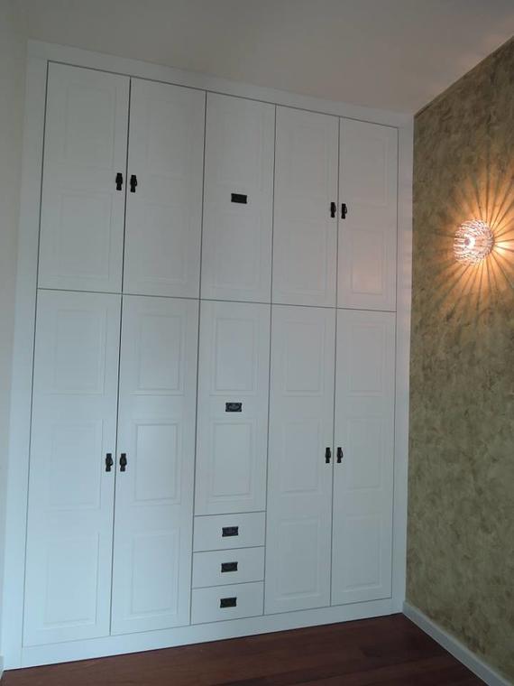 White built-in closet with black handles and drawers against a textured gold wall, next to a wall sconce.