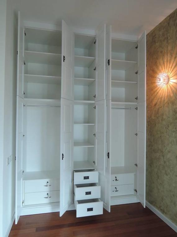 White built-in closet with open doors revealing shelves, hanging rods, and drawers. Wooden floor, golden wall.