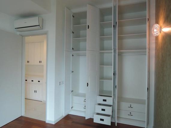 White closet with open doors, interior shelves, and drawers, set in a room with a doorway to another room.