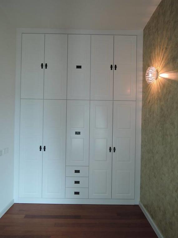 White built-in closet with black handles and three drawers, against a patterned wall, with a wall sconce.