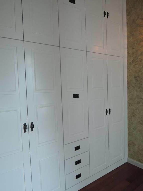 White built-in closet with multiple doors and drawers; black hardware on a wood floor in a room with textured walls.