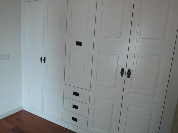 White wardrobe with dark handles and drawers, on a hardwood floor.