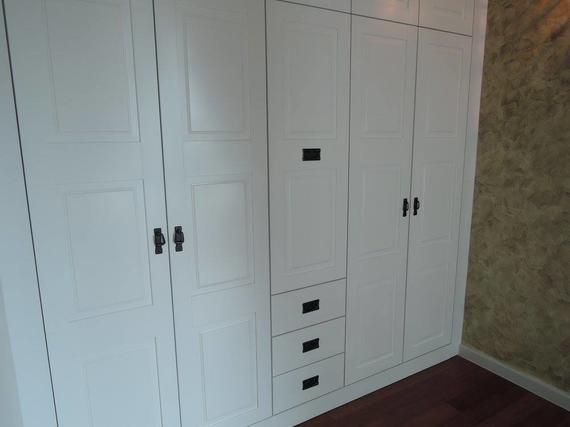 White built-in wardrobe with six doors, three drawers, and black handles. Dark brown floor and textured wall.