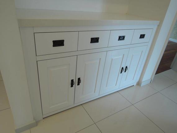White storage cabinet with drawers and doors in a tiled hallway; black hardware.
