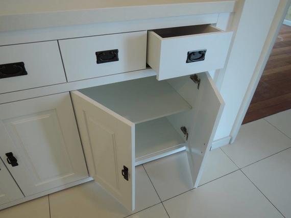 White cabinet with open drawer and door, black hardware, tile floor.