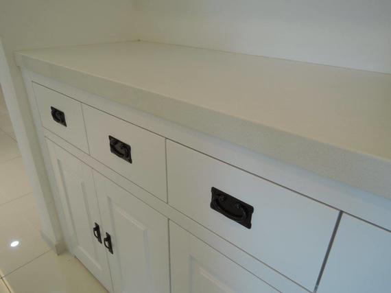 White cabinet with drawers and doors, black handles, set against a white wall.