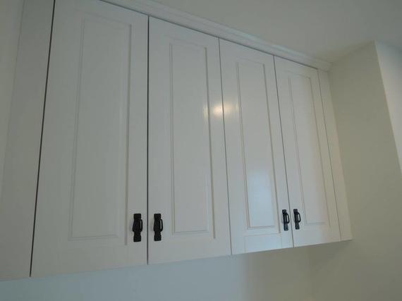 White kitchen cabinets with black handles mounted on a wall.