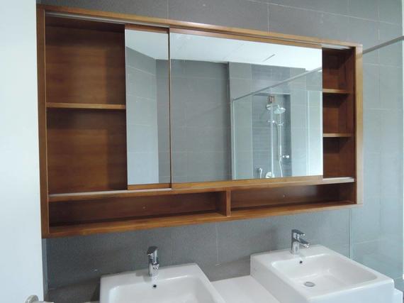 Wooden medicine cabinet with sliding mirror doors, built-in shelves, over two white sinks in a modern bathroom.