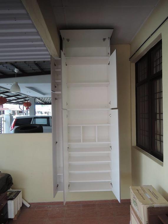 Tall, white cabinet with open doors, mounted on a wall outdoors. Contains shelves, against a tan wall, near a window.