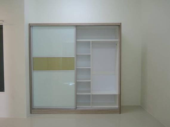 Light-colored wooden wardrobe with sliding glass doors, a shelving unit, and hanging space, against a light beige wall.