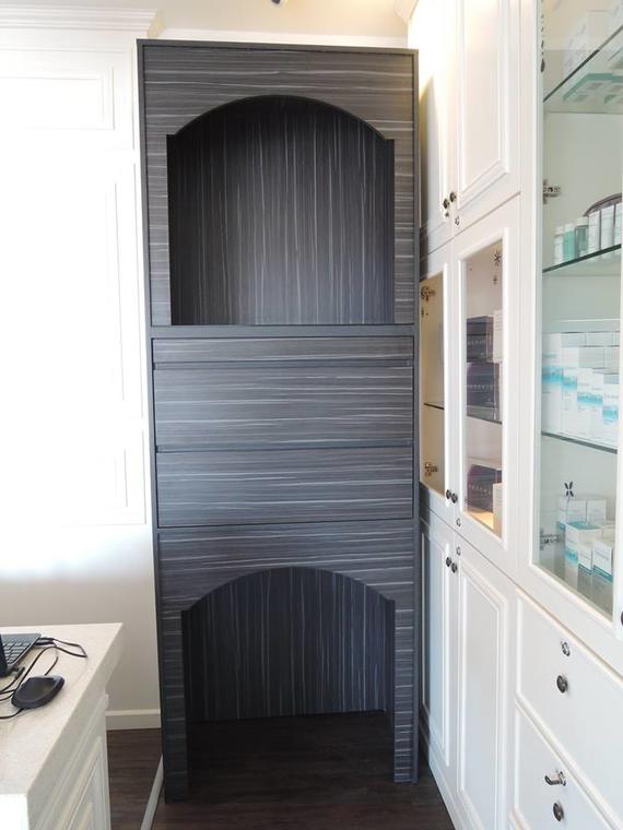 Tall dark gray cabinet with arched top and bottom, built into a white cabinet wall.