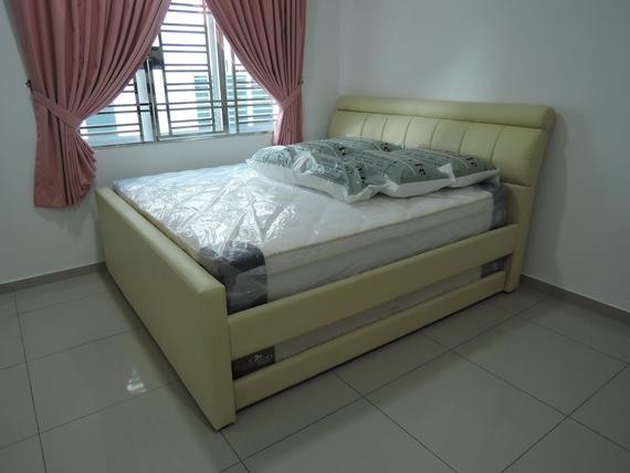 Beige upholstered bed with mattress and pillows, near a window with pink curtains.