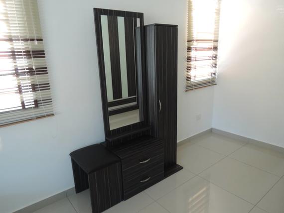 Dark wood vanity with mirror, drawers, stool, and tall cabinet in a bright room.