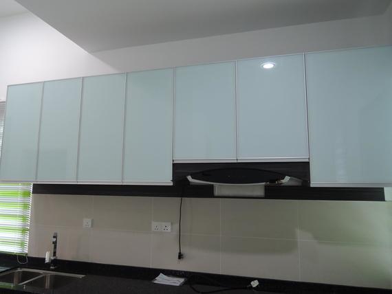 Kitchen cabinets with white glass doors over a black countertop and range hood.