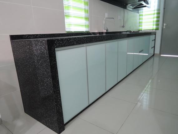Long kitchen countertop with black speckled surface, light blue cabinets, and a window.