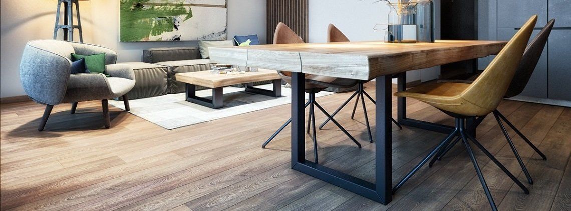 A dining room with a wooden table and chairs. A couch and artwork can be seen in the background.