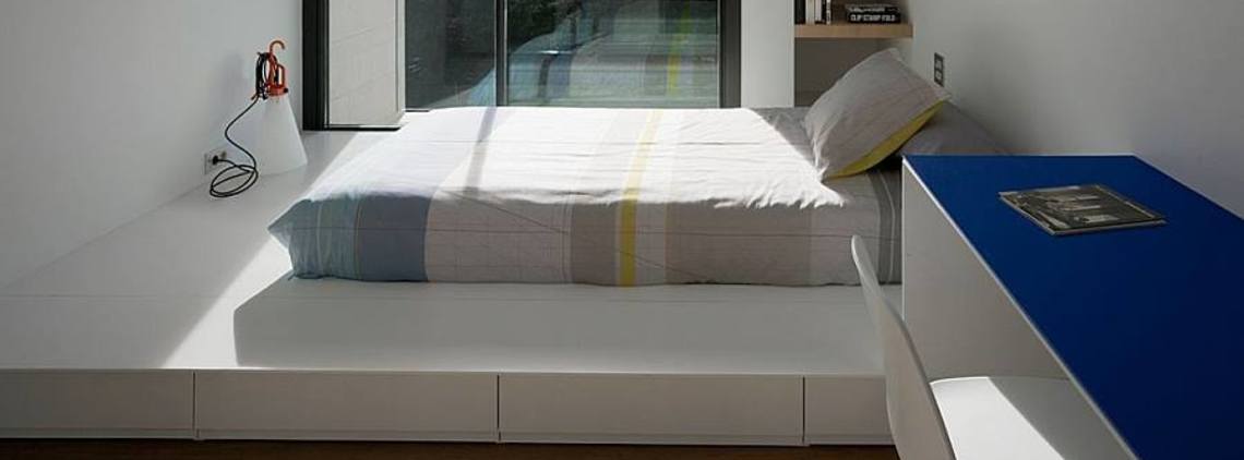 Minimalist bedroom with a bed, white walls, and a blue desk.