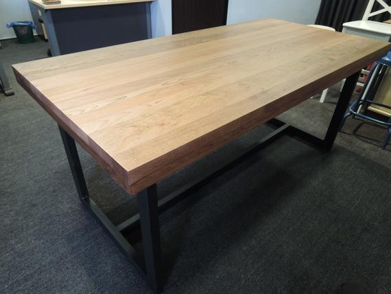 Wooden table with a dark metal base, on gray carpet.